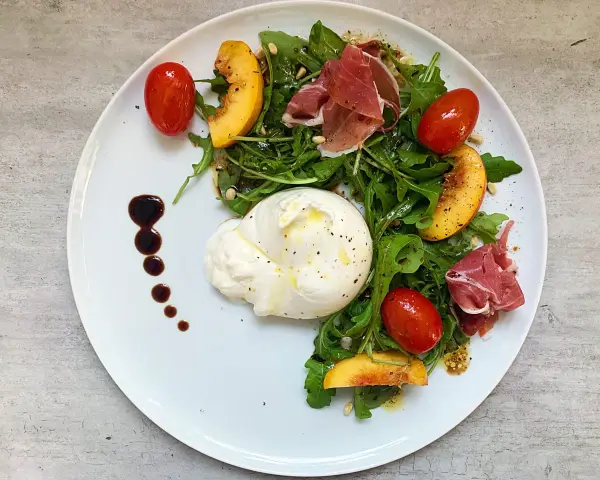 Salat mit Nektarinen, Burrata, Prosciutto und Kirschtomaten, garniert mit Balsamico-Dressing.