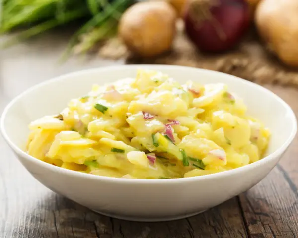 Omas Kartoffelsalat Rezept Original: Ein cremiger Kartoffelsalat mit Zwiebeln und Schnittlauch in einer weißen Schüssel, bereit zum Genießen.