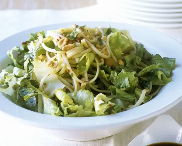 Ein leckerer Yum Yum Salat mit knackigem Eisbergsalat, Nudeln und Erdnüssen in einer weißen Schüssel.