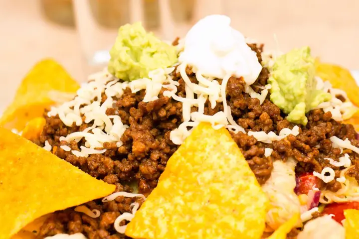 Schichtsalat mit Hackfleisch, Käse, Guacamole und saurer Sahne, garniert mit knusprigen Nachos.
