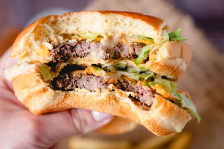 Ein saftiger Burger mit zwei Rindfleisch-Patties, Salat und der unverwechselbaren Big Mac Sauce, gehalten in einer Hand.