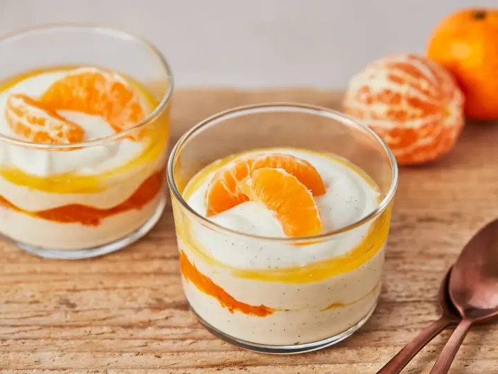 Zwei Gläser mit cremiger Quarkspeise mit Mandarinen, garniert mit frischen Mandarinenspalten.