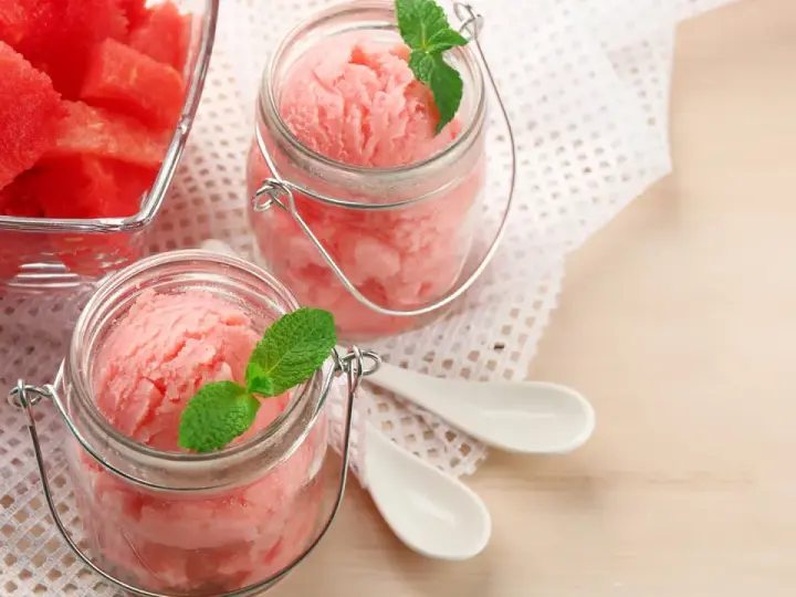 Erfrischendes Meloneneis selber machen: Rosa Sorbet in Gläsern mit Minze, daneben eine Schale mit Wassermelonenwürfeln.