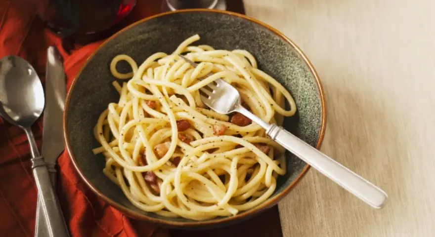 Eine Schüssel Spaghetti mit Speck und Pfeffer, eine köstliche Carbonara ohne Ei, serviert mit einem Glas Rotwein.