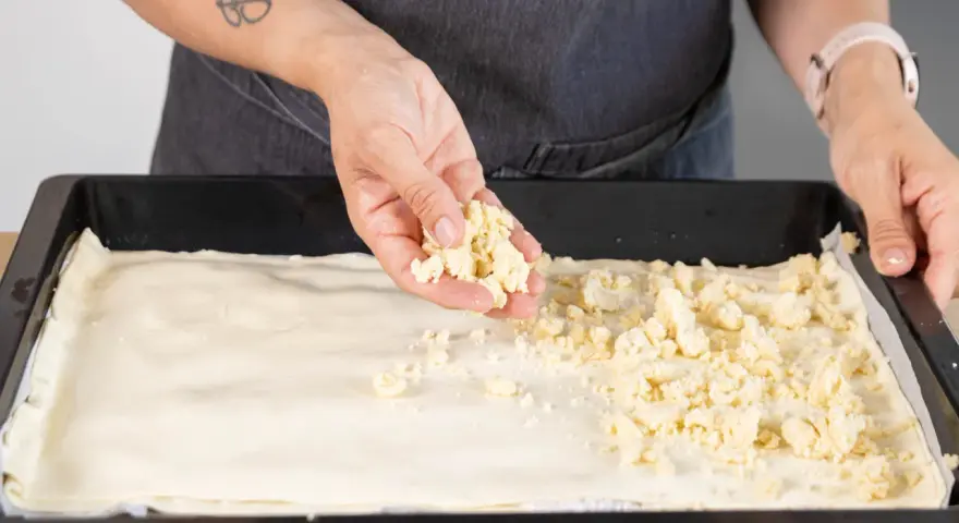 Hände verteilen Streusel auf einem Teigboden für ein Prasselkuchen Rezept DDR.