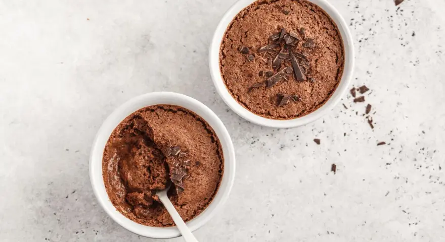 Zwei Schokoladenmousse-Portionen, garniert mit Schokostückchen. Ein Löffel steckt in einer der Schalen, bereit für ein schnelles Dessert.