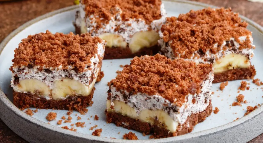 Vier Stücke saftiger Maulwurfkuchen vom Blech mit Bananen und Schokoladenstreuseln auf einem Teller.