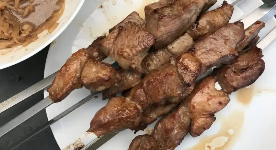 Saftige Fleischspieße, perfekt gegrillt, wie beim besten russischen Schaschlik Rezept. Dazu eine Schüssel mit marinierten Zwiebeln.