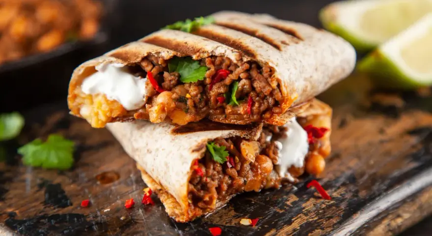 Zwei saftige Burritos, gefüllt mit Hackfleisch, Bohnen und einem Klecks Sauerrahm, sind ein köstliches burrito rezept. Garniert mit Koriander und Chili.