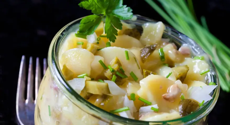 Ein köstlicher Kartoffelsalat ohne Mayo, mit Gurken, Zwiebeln und frischen Kräutern, serviert in einem Glas.