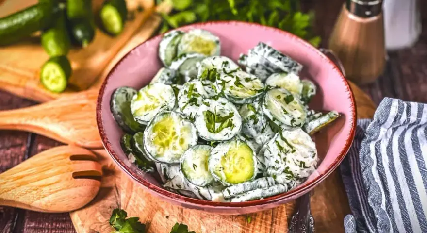 Omas Gurkensalat mit Joghurt, frisch zubereitet und mit Kräutern verfeinert, serviert in einer rosa Schüssel auf einem Holzbrett.