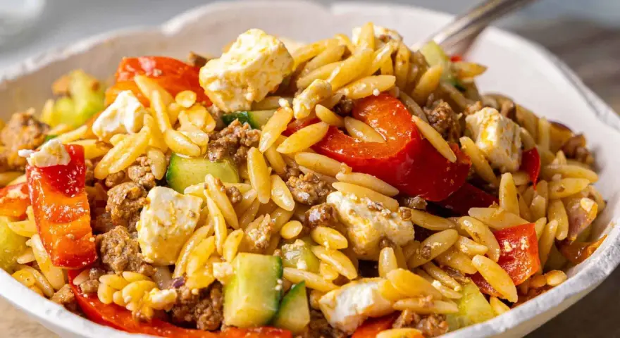 Herzhafter Kritharaki Salat mit Hackfleisch, Feta, Gurke und roten Paprikastücken. Ein köstliches Gericht, das alle Geschmacksnerven verwöhnt.