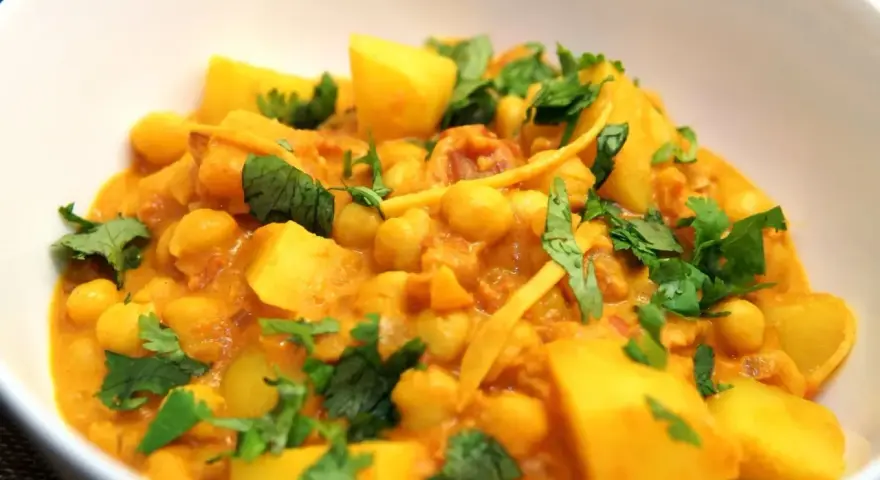 Herzhaftes Kichererbsen Curry mit Kartoffelstücken und frischem Koriander, ein Genuss für die Sinne.