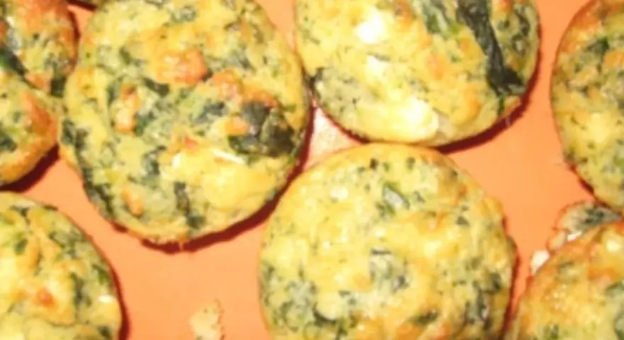 Saftige Spinat Feta Muffins, goldbraun gebacken, mit sichtbaren grünen Spinatstückchen und weißen Feta-Käse-Einlagen.
