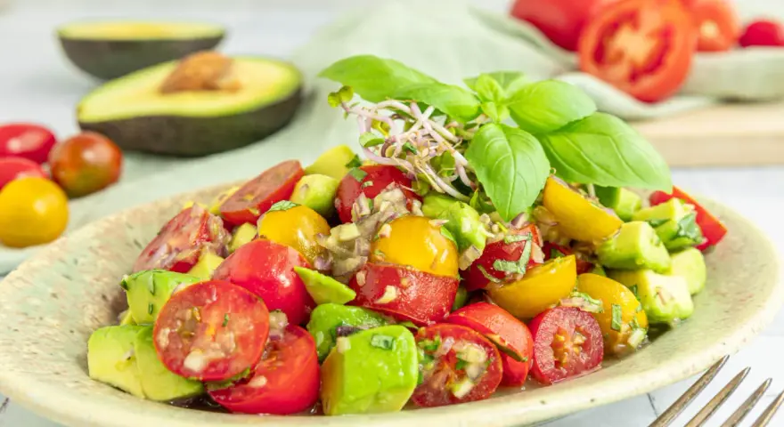 Frischer Avocado Tomaten Salat mit Basilikum und Sprossen, garniert mit roten und gelben Kirschtomaten.