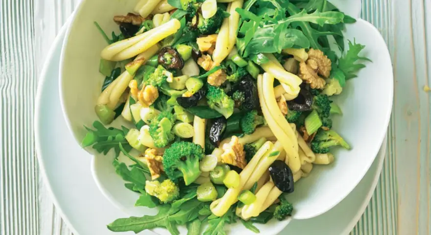 Frischer nudelsalat mit brokkoli, Walnüssen, Oliven und Rucola in einer weißen Schüssel.