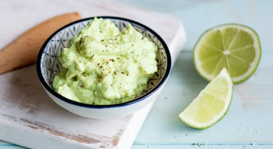 Cremiger Avocado Feta Dip, gewürzt mit Pfeffer, daneben frische Limettenspalten. Perfekt zum Dippen!