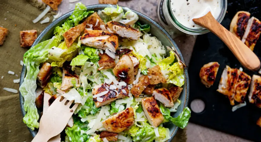 Frischer Caesar Salat mit gegrilltem Hähnchen, Croutons und Parmesan. Dazu ein Glas mit cremigem Caesar Salat Dressing.
