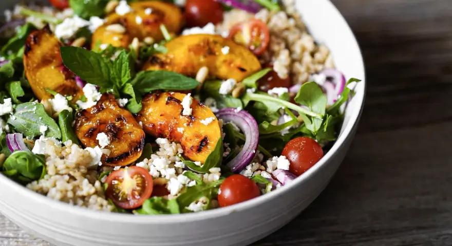 Ein bunter Pfirsich Feta Salat mit gegrillten Pfirsichspalten, Kirschtomaten, Rucola und Getreide.