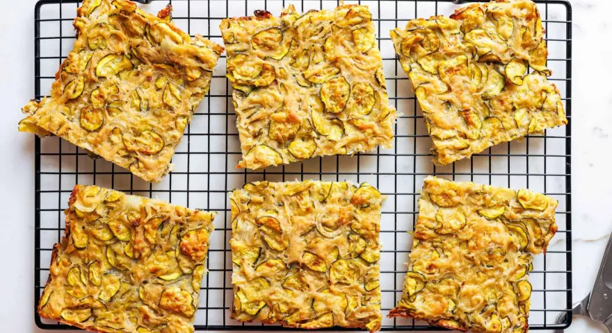 Sechs rechteckige Stücke Zucchini Scarpaccia liegen auf einem schwarzen Gitterrost.