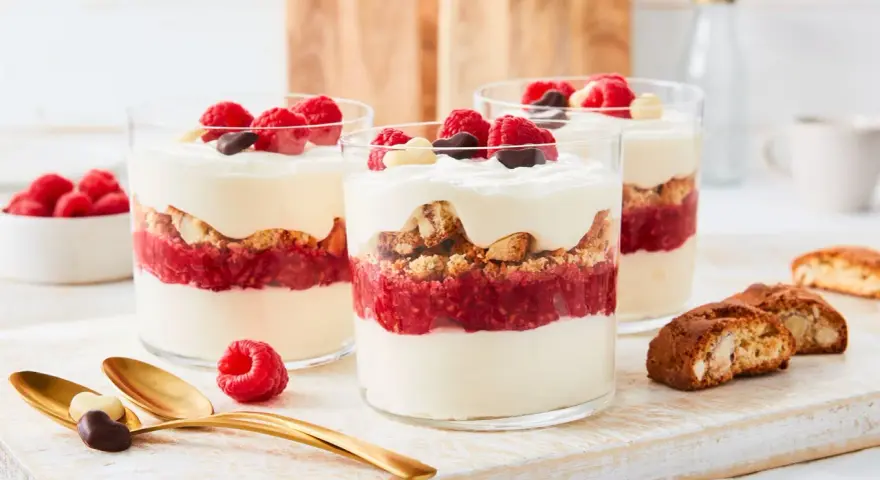 Schichtdessert mit Himbeeren, knusprigen Keksen und cremigem **dessert mit mascarpone**, garniert mit frischen Beeren und Schokolade.