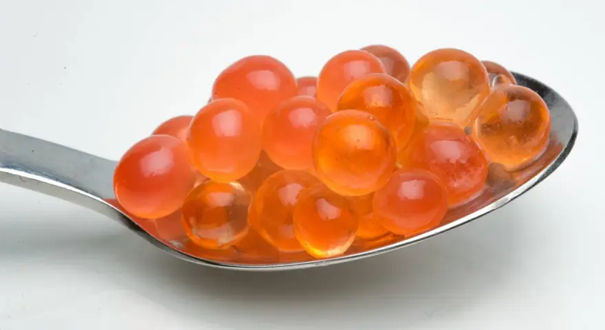 Löffel voller leuchtend oranger Kugeln, die aussehen, als könnte man sie leicht selber machen. Tapioka perlen selber machen ist einfacher als gedacht!