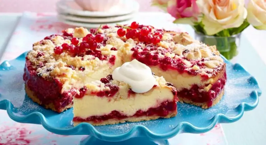 Saftiger Johannisbeerkuchen mit Quark und Streuseln, garniert mit frischen roten Johannisbeeren und einem Klecks Sahne.
