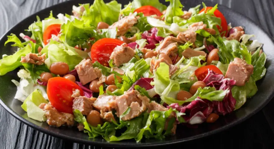 Frischer Thunfischsalat mit knackigem Salat, Tomaten und Bohnen auf schwarzem Teller.