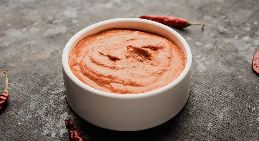 Eine Schale mit cremiger Piri Piri Sauce, umgeben von getrockneten Chilis auf dunklem Untergrund.