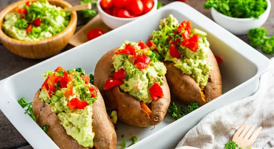 Gefüllte Süßkartoffeln mit Avocado-Topping. Leckere, kalte Rezepte mit Avocado, garniert mit Paprika und Kräutern.