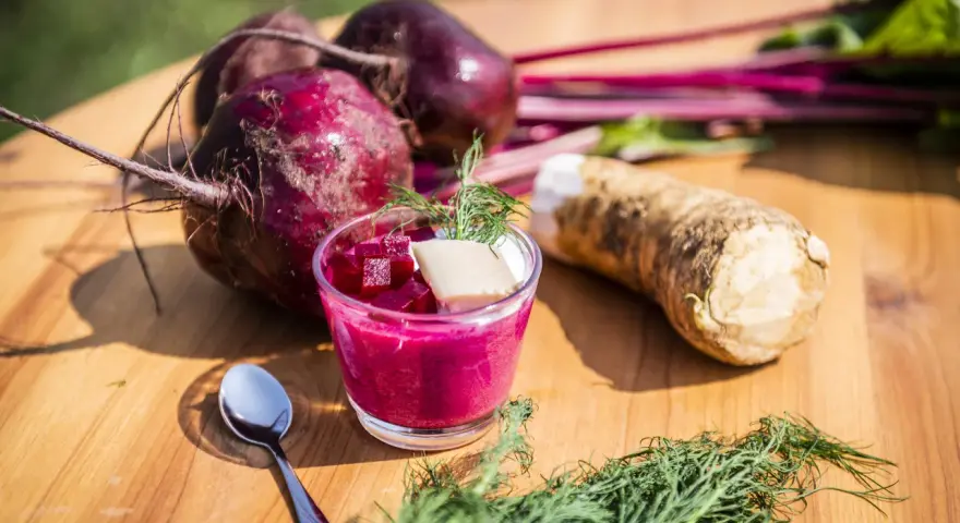 Rote Bete Mus Rezept: Frische rote Bete, Meerrettich und Dill auf Holztisch. Ein Glas mit leuchtend pinkem Mus, garniert mit Würfeln und Dill.