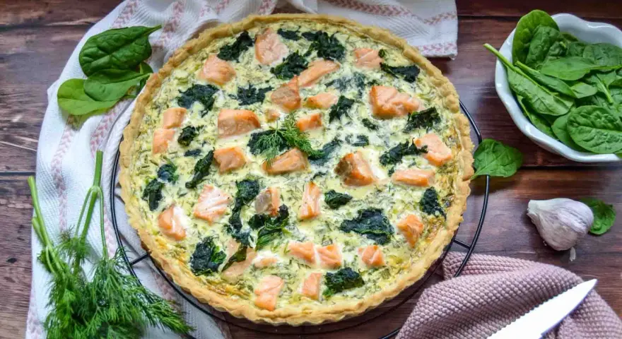 Herzhafte Spinat Lachs Quiche mit frischem Dill garniert, bereit zum Servieren.