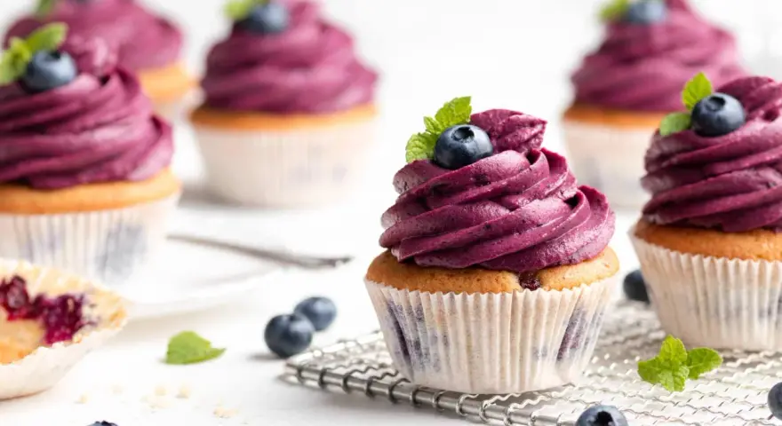Mehrere Muffins mit lila Beeren-Topping, garniert mit frischen Blaubeeren und Minze. Ein einfacher, köstlicher Genuss.
