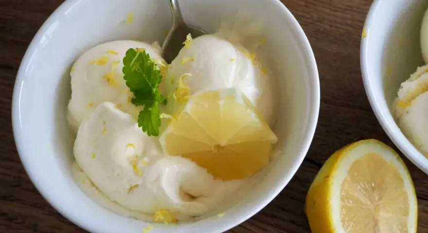 Erfrischendes zitroneneis selber machen: Cremiges Eis in einer Schüssel, garniert mit Zitronenspalte und Minze.