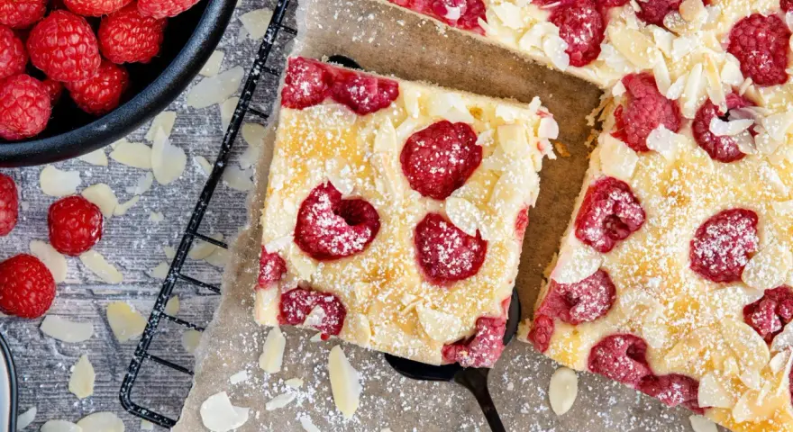 Schneller Kuchen mit gefrorenen Himbeeren, bestreut mit Puderzucker und Mandelblättchen. Ein Genuss für jeden Anlass!