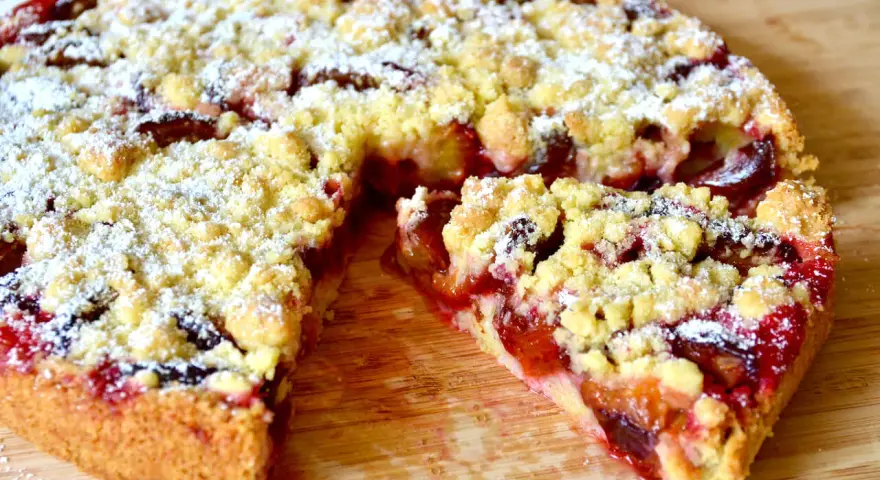 Saftiger pflaumenkuchen ohne hefe springform, mit Streuseln und Puderzucker bestäubt, auf einem Holzbrett.