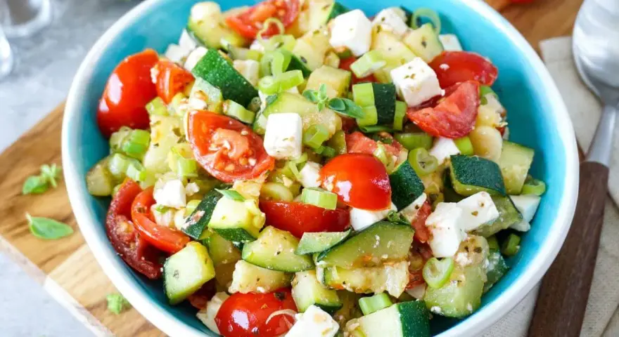 Erfrischender Zucchini Salat mit Tomaten, Feta und Frühlingszwiebeln, garniert mit frischen Kräutern. Ein leichter Genuss.