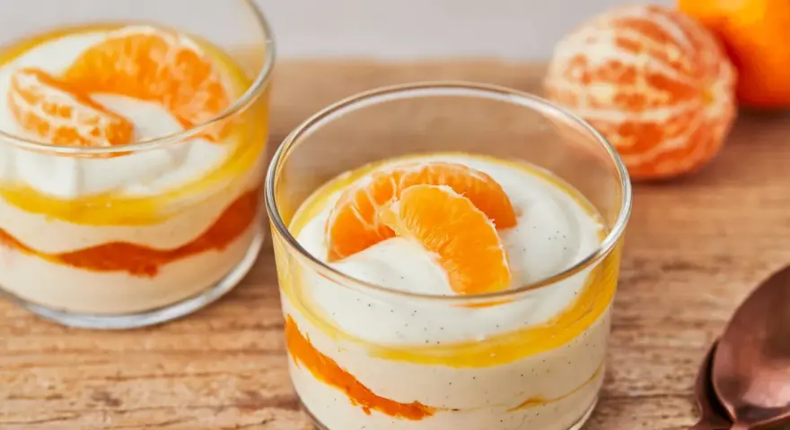 Zwei Gläser mit cremiger Quarkspeise mit Mandarinen, garniert mit frischen Mandarinenspalten.