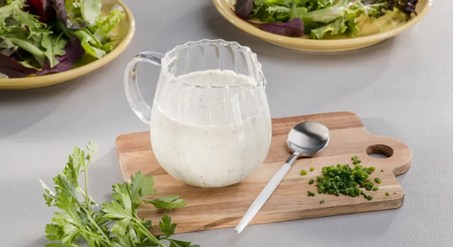 Ein Krug mit cremigem Ranch Dressing, daneben Schnittlauch und Petersilie. Perfekt für einen frischen Salat.