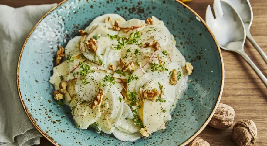 Ein erfrischender rettichsalat mit apfel, garniert mit Walnüssen und Petersilie, auf einem türkisfarbenen Teller.