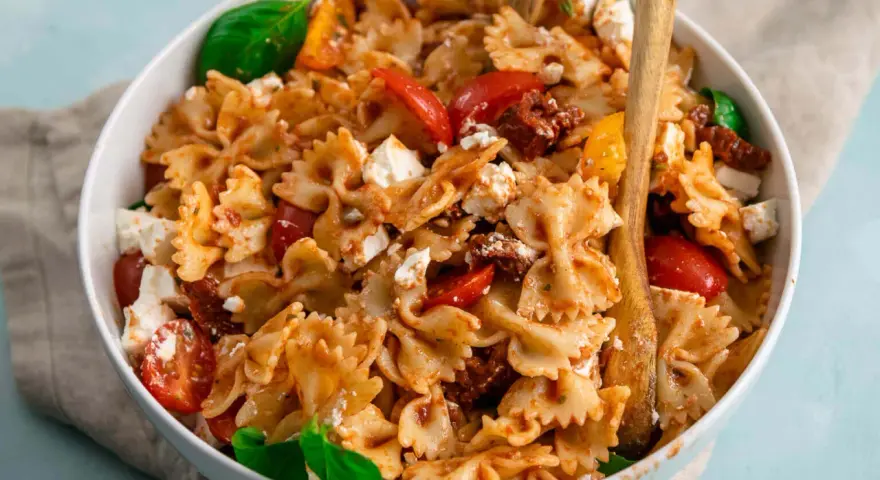 Ein köstlicher Nudelsalat mit Farfalle, frischen Tomaten, Mozzarella und sonnengetrockneten Tomaten, garniert mit Basilikum.