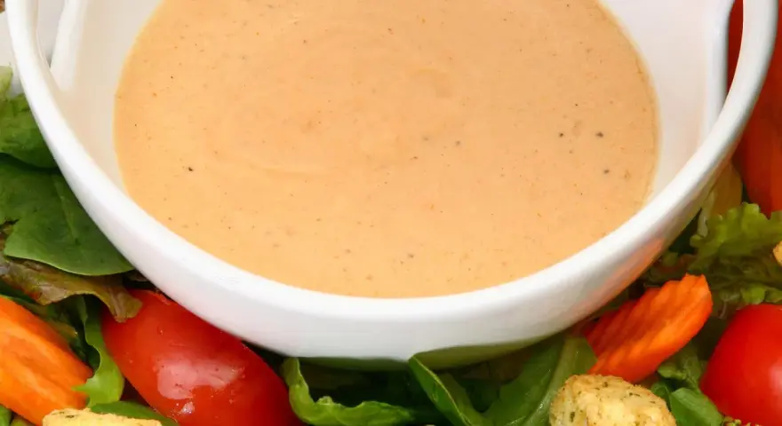 Cremiges French Dressing in einer weißen Schüssel, umgeben von frischem Salat, Tomaten und Karotten.