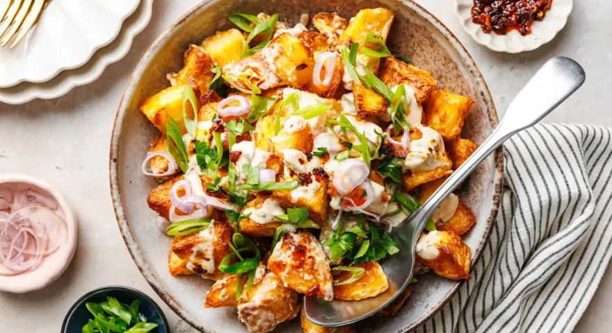 Kartoffelsalat mal anders: knusprige Kartoffelspalten mit cremiger Sauce, Frühlingszwiebeln und roten Zwiebelringen in einer rustikalen Schüssel.