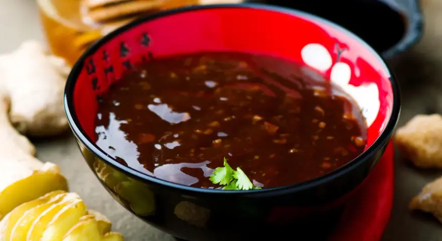Schwarze Schüssel mit glänzender Teriyaki-Sauce, umgeben von Ingwer, Knoblauch und Chili. Ein köstliches teriyaki sauce rezept zum Nachkochen.