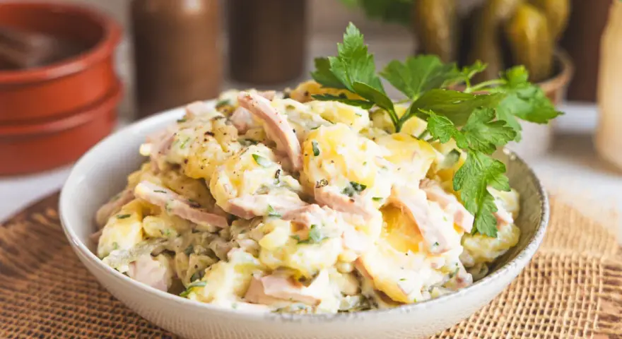 Schüssel mit Kartoffelsalat mit Miracel Whip, Schinken und Petersilie. Dazu passen Gewürzgurken.