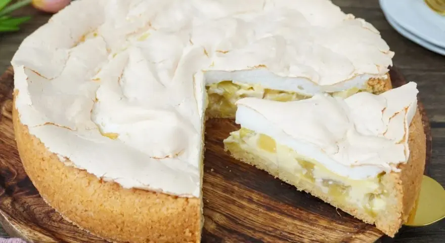 Ein saftiger Rhabarberkuchen mit luftigem Baiser, ein Stück davon ist bereits angeschnitten.