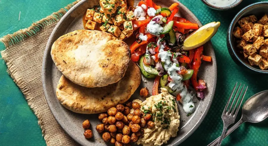 Ein bunter griechischer Salat mit Hummus, gerösteten Kichererbsen und Pitabrot. Dazu gewürfelter Tofu und ein Zitronenschnitz.