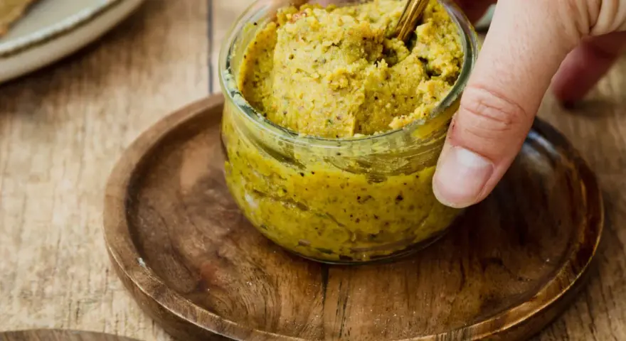 Ein Glas mit selbstgemachter Pistaziencreme, die mit einem goldenen Löffel umgerührt wird. Perfekt zum Brot oder als Dip.