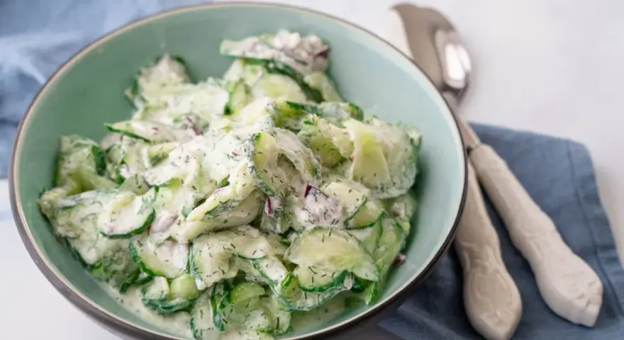 Frischer gurkensalat mit saurer sahne, garniert mit Dill und roten Zwiebeln, serviert in einer hellgrünen Schüssel.