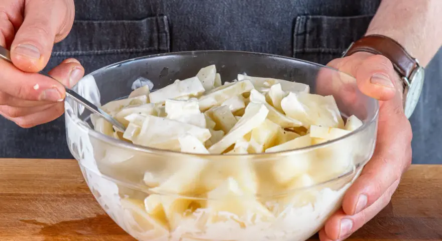 Hände mischen in einer Glasschüssel den cremigen selleriesalat nach Omas Rezept.